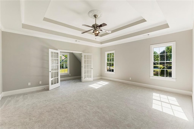 carpeted spare room featuring french doors, ceiling fan, a tray ceiling, and a wealth of natural light