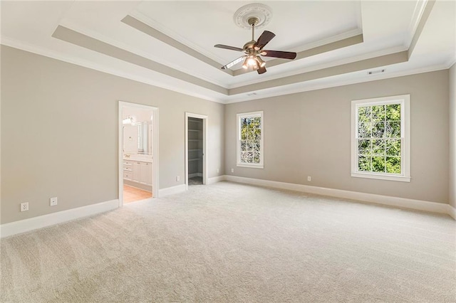 unfurnished bedroom featuring light carpet, connected bathroom, ceiling fan, and a tray ceiling