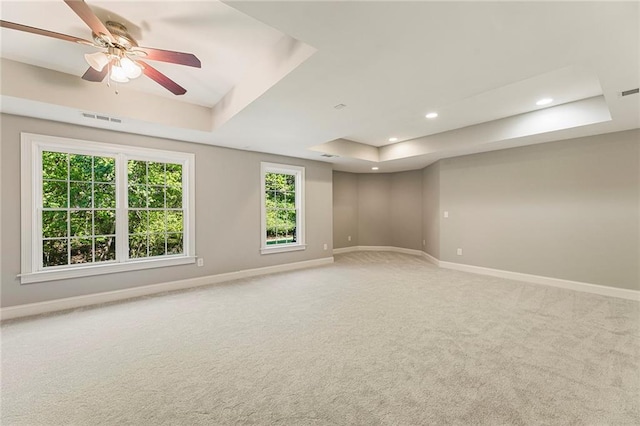 carpeted empty room featuring ceiling fan, a raised ceiling, and a healthy amount of sunlight