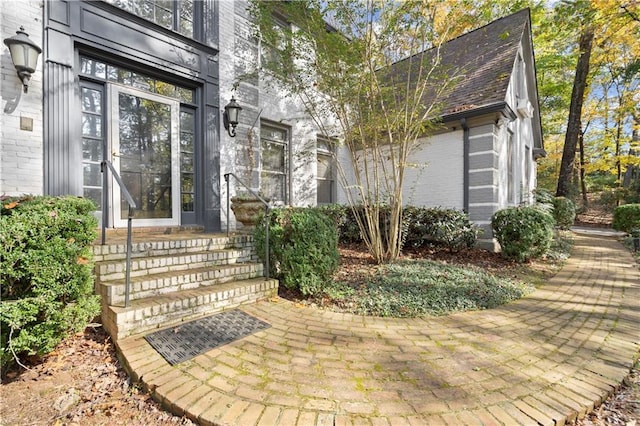 doorway to property featuring a shingled roof and brick siding