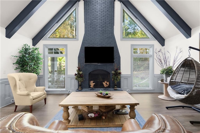 living room featuring vaulted ceiling with beams, a wainscoted wall, and a brick fireplace