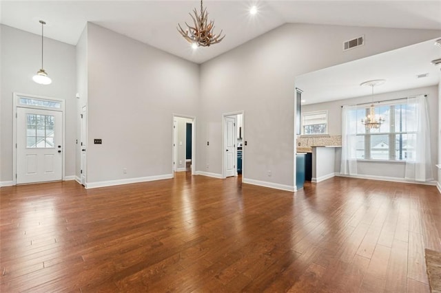 unfurnished living room featuring an inviting chandelier, dark wood-type flooring, and high vaulted ceiling