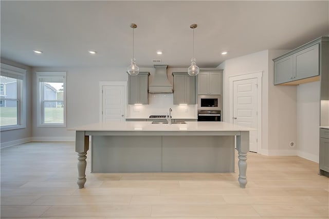 kitchen featuring gray cabinetry, custom exhaust hood, stainless steel appliances, sink, and an island with sink