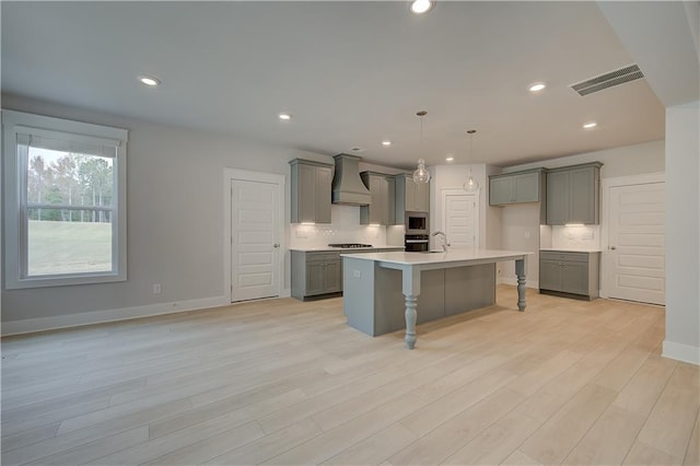 kitchen with premium range hood, gray cabinets, light hardwood / wood-style flooring, and an island with sink