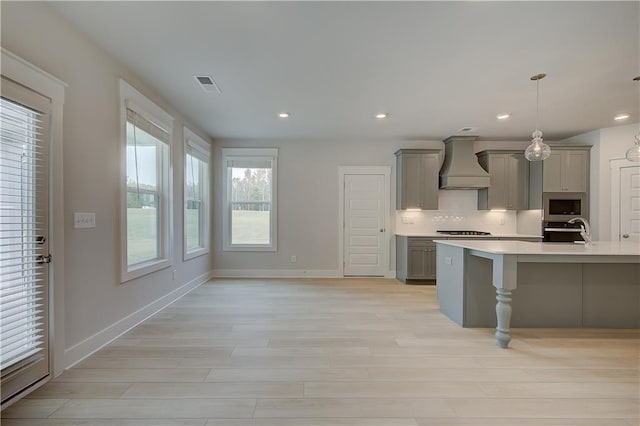 kitchen with gray cabinetry, hanging light fixtures, decorative backsplash, custom exhaust hood, and appliances with stainless steel finishes