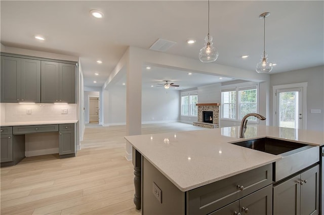 kitchen with ceiling fan, sink, a kitchen island with sink, light hardwood / wood-style flooring, and decorative backsplash