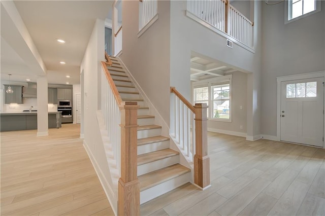 entrance foyer with a towering ceiling, coffered ceiling, sink, beamed ceiling, and light hardwood / wood-style floors