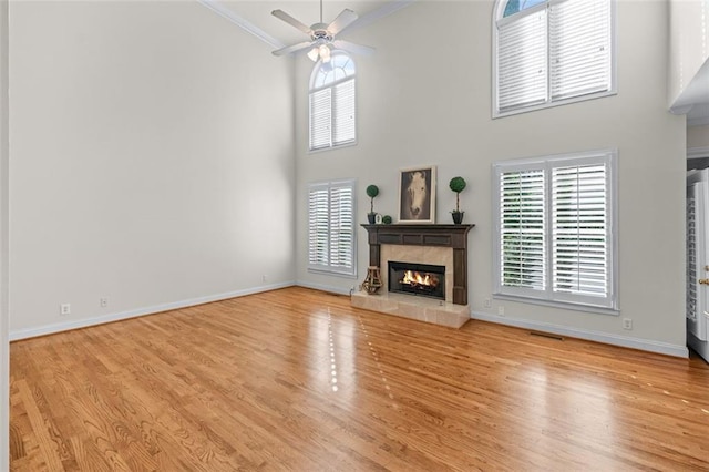 unfurnished living room with crown molding, a tile fireplace, baseboards, wood finished floors, and a towering ceiling