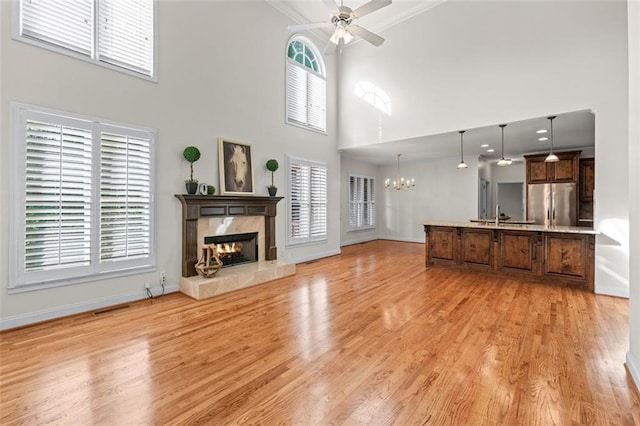unfurnished living room featuring a tiled fireplace, plenty of natural light, ceiling fan with notable chandelier, and baseboards