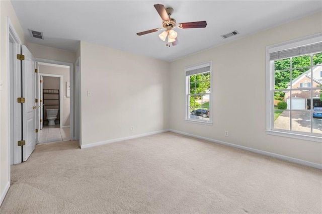 empty room with baseboards, light carpet, a ceiling fan, and visible vents