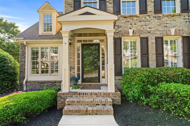 doorway to property with brick siding and roof with shingles