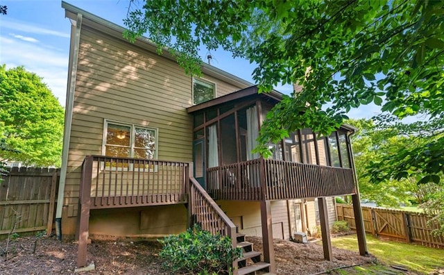 rear view of house with a wooden deck, a fenced backyard, a sunroom, and stairs