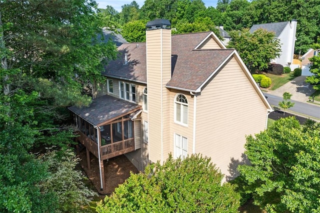 back of house with a shingled roof, a chimney, and a sunroom