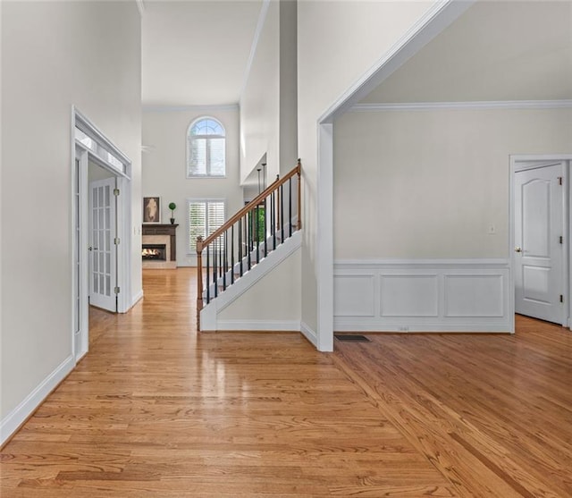 entrance foyer featuring a warm lit fireplace, ornamental molding, light wood finished floors, and stairway