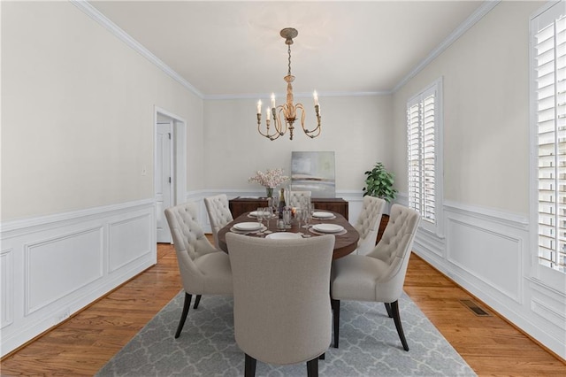 dining area with wood finished floors, a wainscoted wall, crown molding, visible vents, and a chandelier