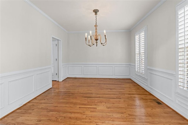 unfurnished dining area with visible vents, crown molding, light wood-type flooring, a wainscoted wall, and a chandelier