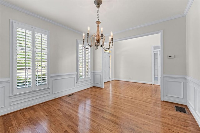 unfurnished dining area with crown molding, a notable chandelier, light wood-style flooring, a wainscoted wall, and visible vents