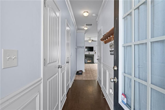 hall featuring dark wood-style floors, a wainscoted wall, visible vents, a decorative wall, and ornamental molding