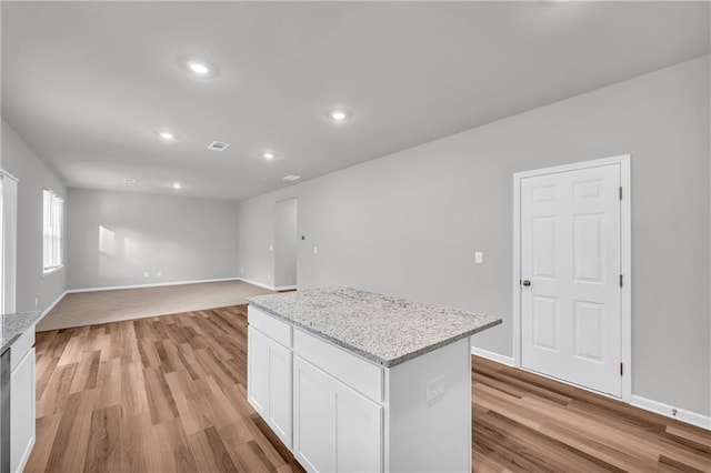 kitchen featuring light stone counters, white cabinets, light wood-type flooring, and a kitchen island