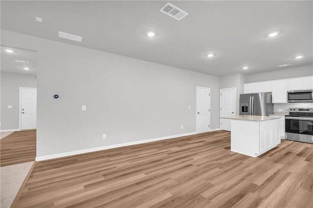 kitchen with light hardwood / wood-style floors, light stone countertops, appliances with stainless steel finishes, white cabinets, and a kitchen island