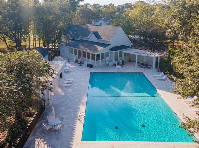 rear view of house with a community pool, a patio area, a pergola, and a sunroom