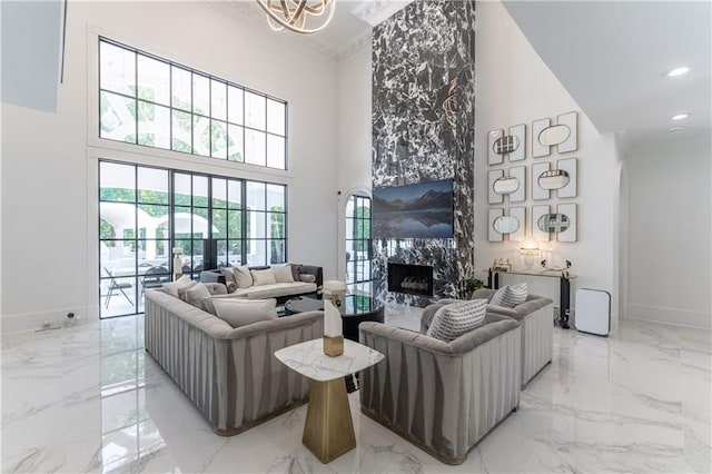 living area featuring a high end fireplace, baseboards, ornamental molding, a towering ceiling, and marble finish floor