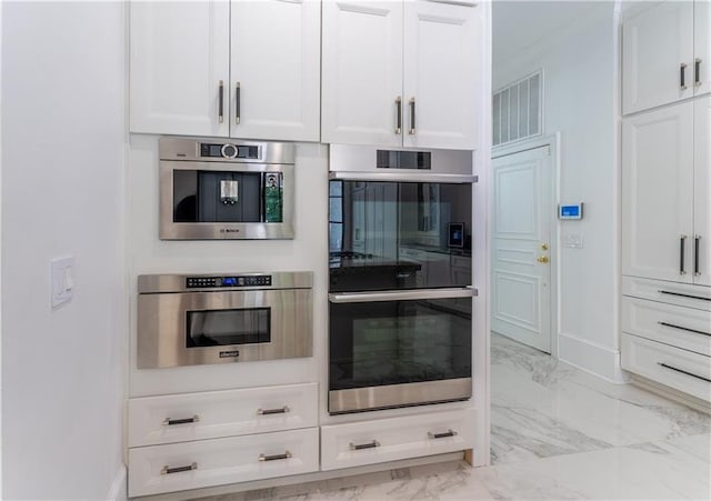 kitchen featuring visible vents, baseboards, white cabinets, stainless steel double oven, and marble finish floor