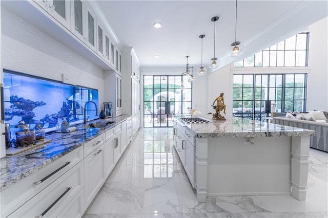 kitchen with marble finish floor, light stone counters, a sink, white cabinets, and glass insert cabinets