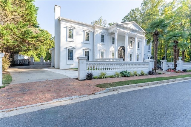 greek revival house featuring a fenced front yard, decorative driveway, a porch, and stucco siding