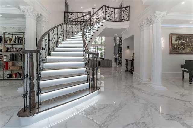 entrance foyer featuring marble finish floor, crown molding, a towering ceiling, and decorative columns