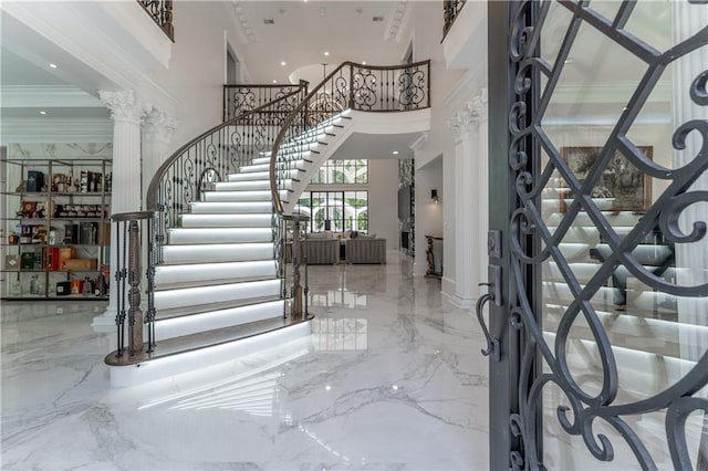 foyer entrance featuring stairway, decorative columns, a towering ceiling, crown molding, and marble finish floor