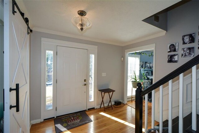 entryway featuring hardwood / wood-style flooring, crown molding, a barn door, and plenty of natural light