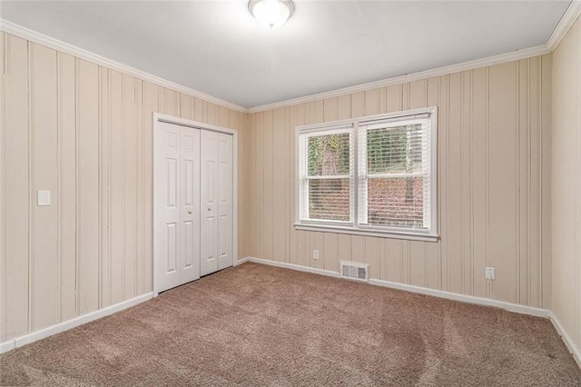 unfurnished bedroom featuring carpet, visible vents, baseboards, a closet, and crown molding