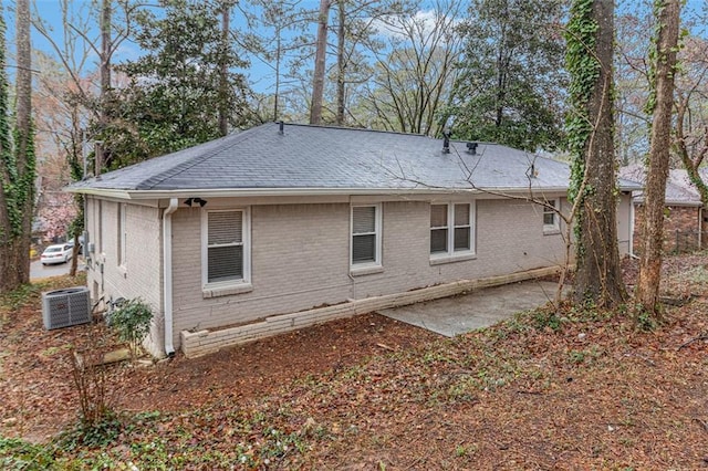 back of house featuring central air condition unit, a patio, brick siding, and roof with shingles