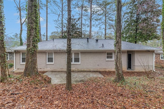 rear view of property with brick siding, a shingled roof, and a patio