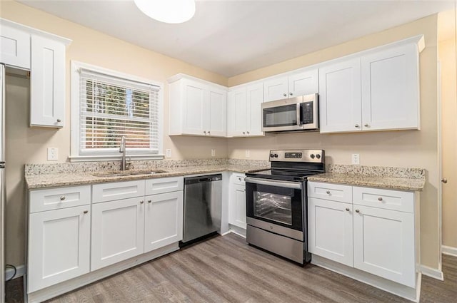 kitchen with light wood-style flooring, a sink, light stone counters, stainless steel appliances, and white cabinets