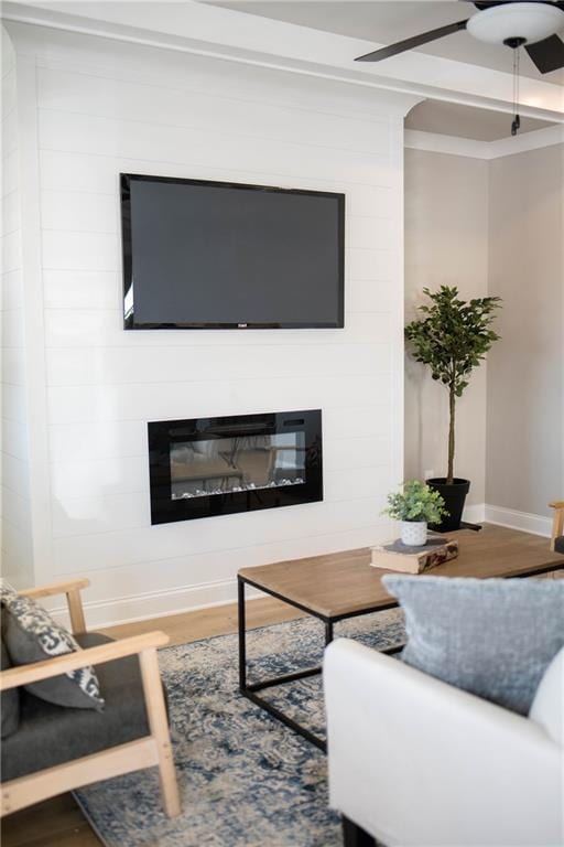 living area featuring a fireplace, a ceiling fan, baseboards, and wood finished floors