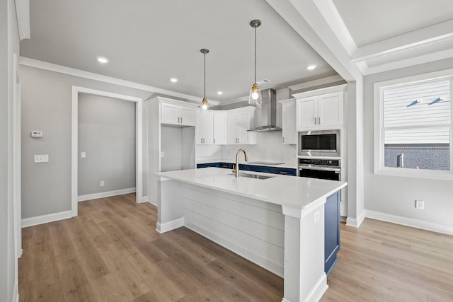 kitchen with a sink, wall chimney range hood, stainless steel appliances, white cabinets, and light countertops