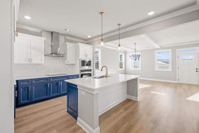 kitchen featuring built in microwave, a sink, stainless steel oven, wall chimney range hood, and blue cabinets