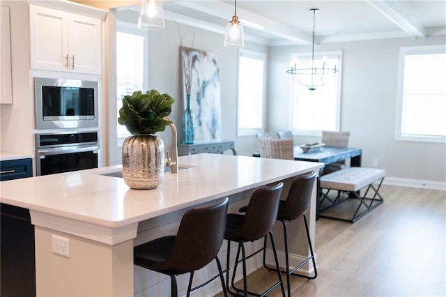 kitchen with beamed ceiling, plenty of natural light, light wood-style flooring, and appliances with stainless steel finishes