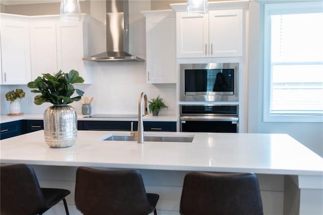 kitchen with light countertops, a kitchen breakfast bar, stainless steel appliances, wall chimney exhaust hood, and a sink