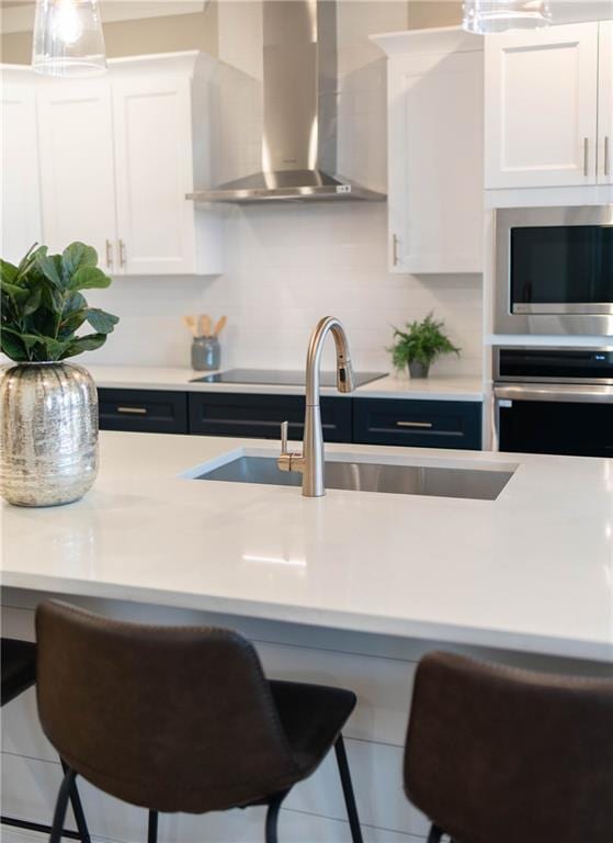 kitchen with light countertops, a kitchen breakfast bar, stainless steel appliances, wall chimney exhaust hood, and a sink