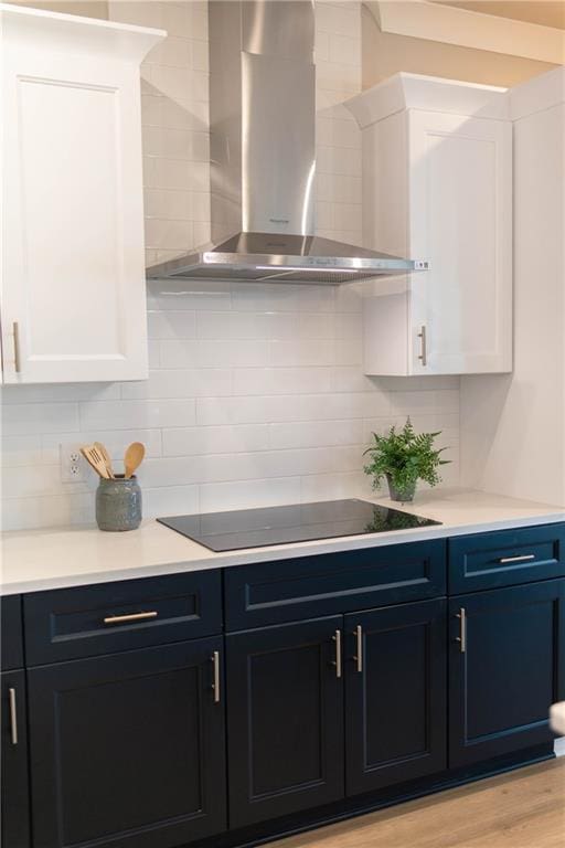 kitchen featuring white cabinetry, wall chimney range hood, black electric cooktop, and backsplash