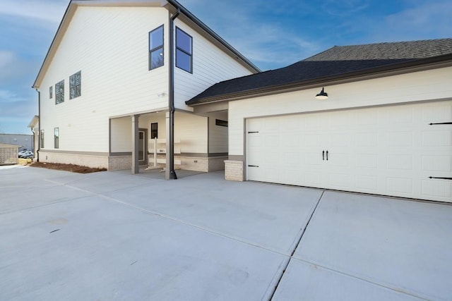 exterior space with an attached garage, concrete driveway, and roof with shingles