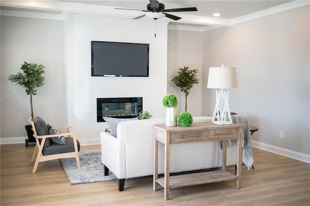 living room featuring a ceiling fan, baseboards, ornamental molding, light wood-style floors, and a large fireplace