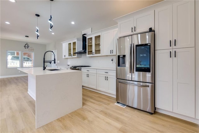 kitchen with hanging light fixtures, wall chimney range hood, stainless steel fridge with ice dispenser, a center island with sink, and white cabinets