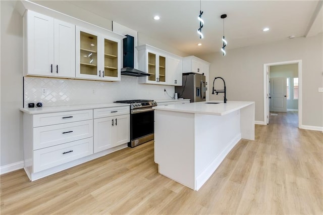 kitchen with wall chimney exhaust hood, hanging light fixtures, stainless steel appliances, a kitchen island with sink, and light wood-type flooring