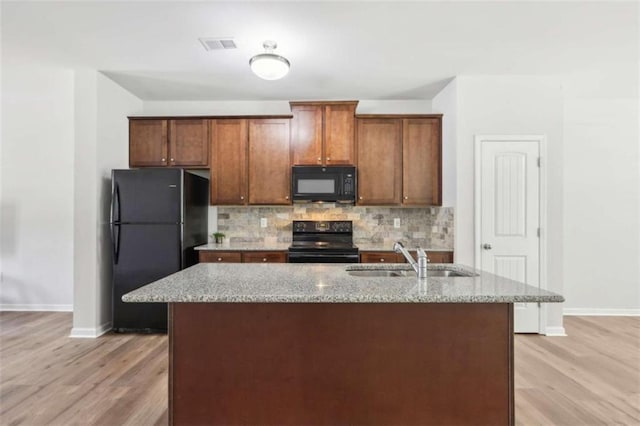 kitchen featuring sink, black appliances, light stone countertops, a kitchen island with sink, and backsplash