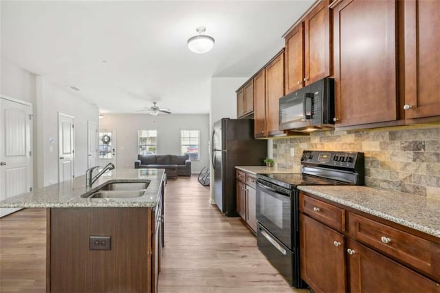 kitchen with sink, backsplash, black appliances, an island with sink, and light stone countertops