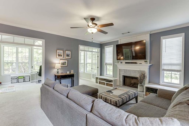 carpeted living area featuring a large fireplace, a ceiling fan, crown molding, and visible vents